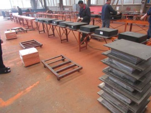 Workers are assembling all parts of the natural rubber bearing into a whole unit.